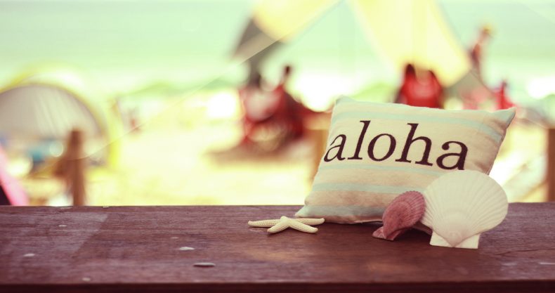 alohaと書かれたミニクッションの後ろには綺麗な海